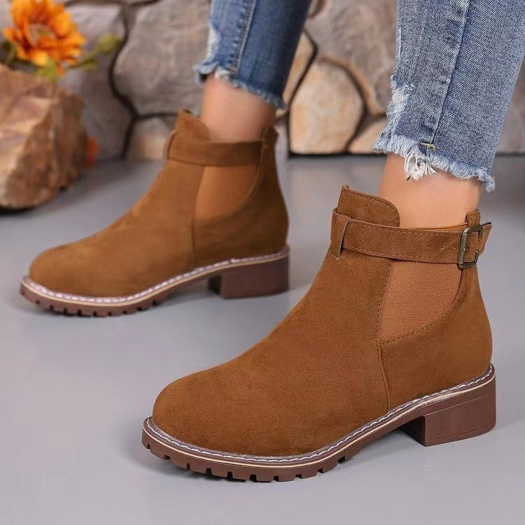 Braune Chelsea Boots mit Absatz und Schnalle vor Steinwand-Hintergrund