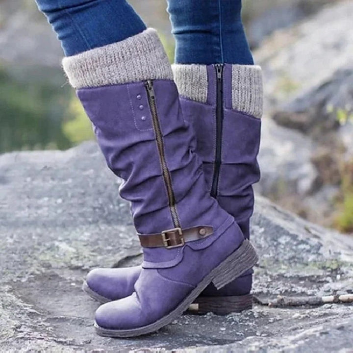 Violette Kniestiefel mit Strickbund und Schnallenriemen am Fuß getragen