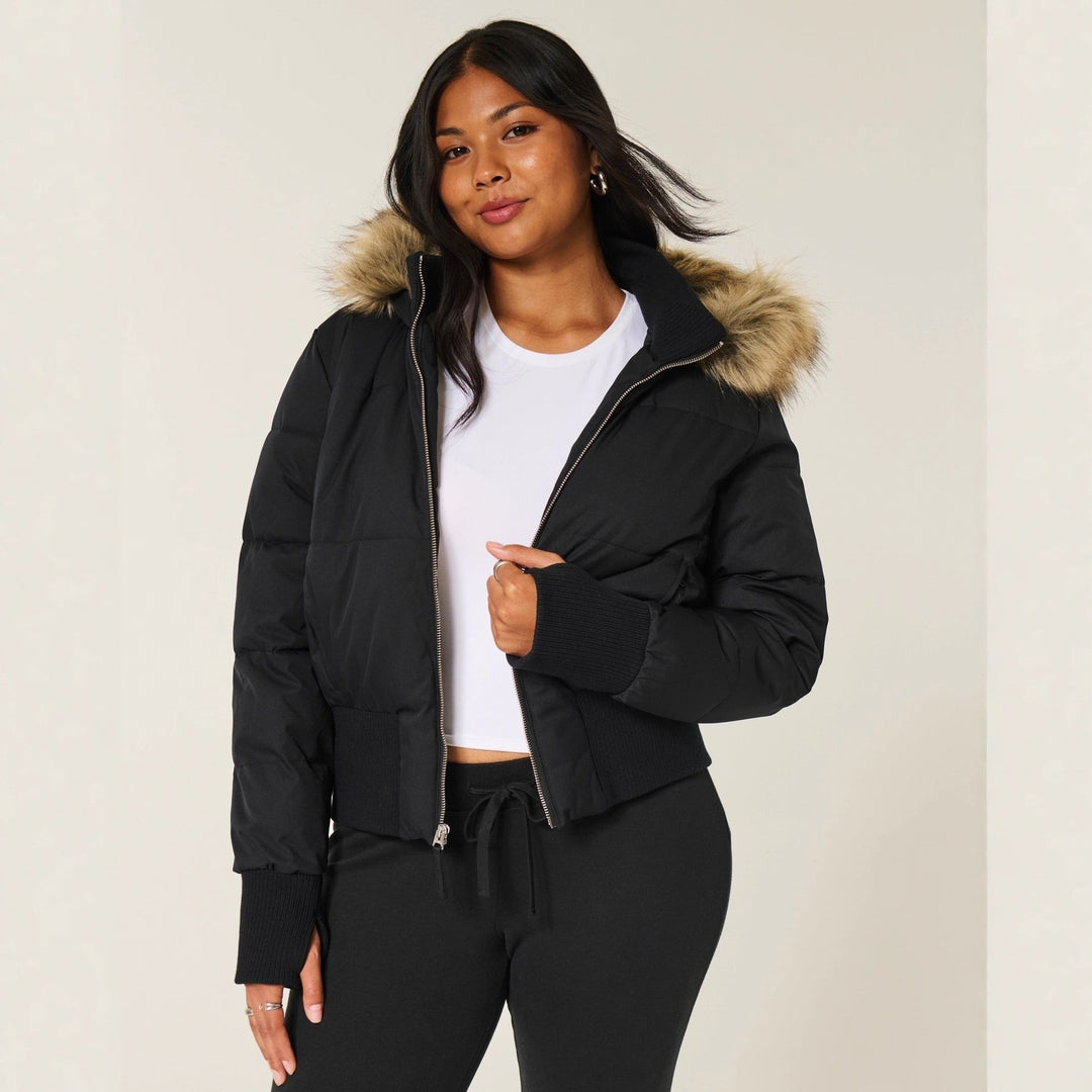 Schwarze Cropped Steppjacke mit Kunstfellkapuze über weißem Top getragen