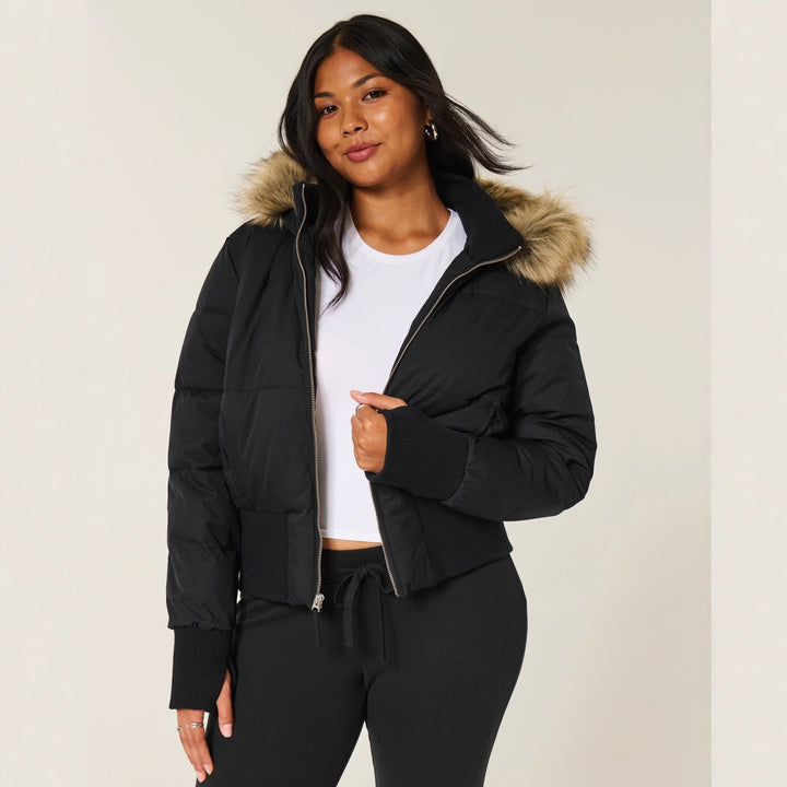 Schwarze Cropped Steppjacke mit Kunstfellkapuze über weißem Top getragen