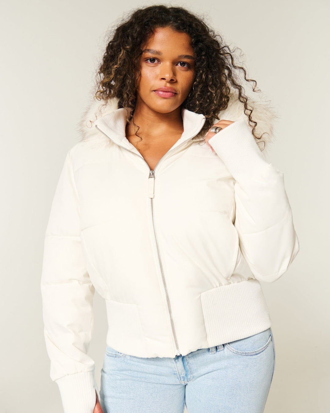 Cremeweiße Steppjacke mit Kunstfellkapuze und Rippbündchen zu heller Jeans