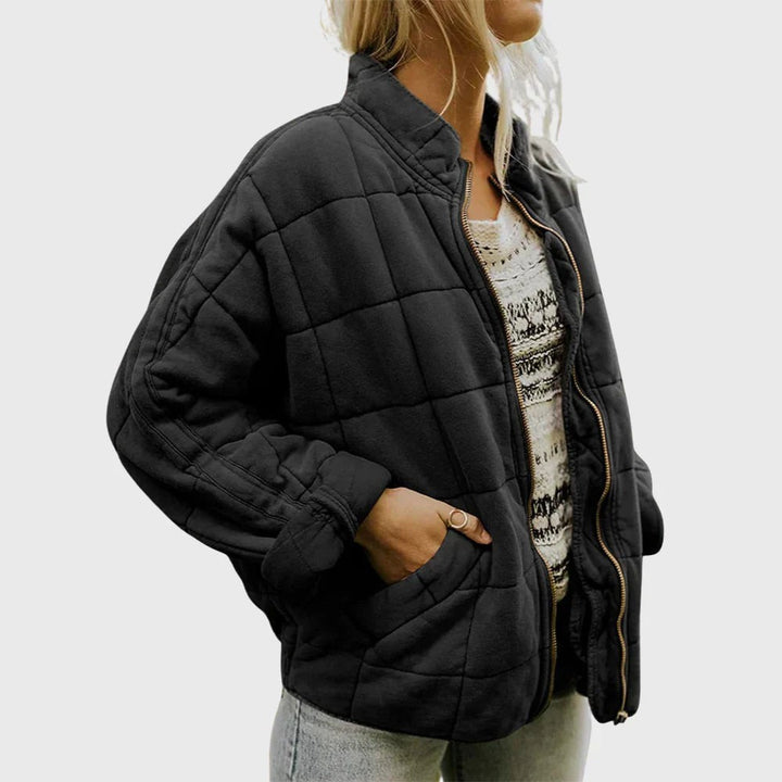 Schwarze Steppjacke mit Stehkragen, offen getragen über gemustertem Pullover