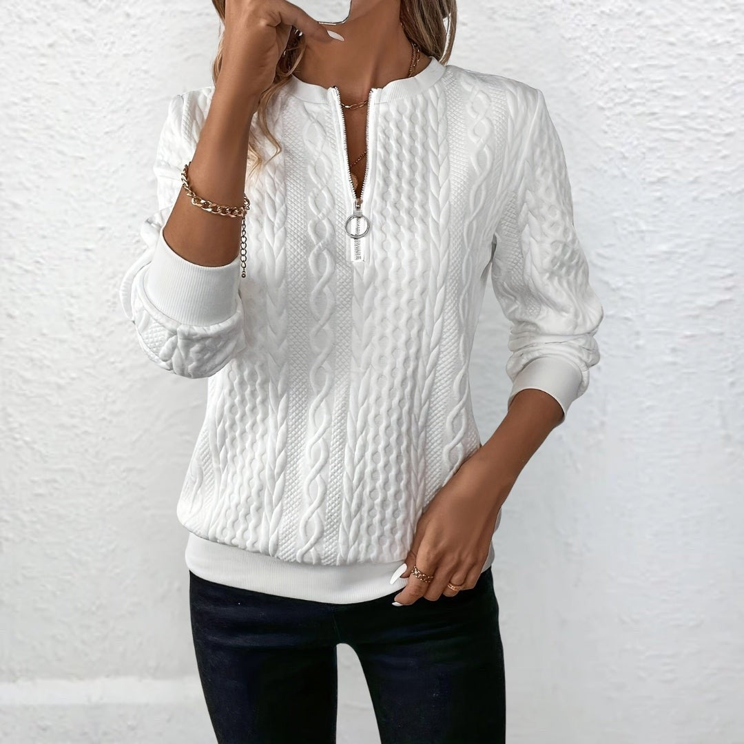 Weißer Strickpullover mit Zopfmuster und Reißverschluss-Ausschnitt vor heller Wand