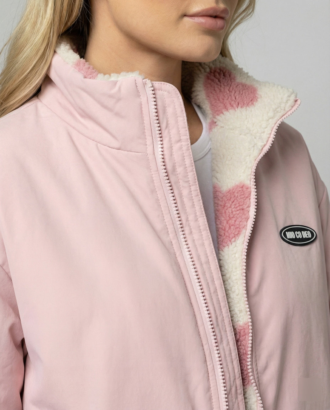 Detailaufnahme des Stehkragens mit rosa Herzmuster-Teddyfutter und Logo-Patch