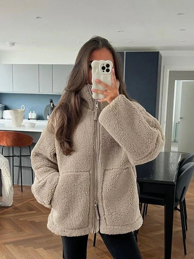 Frau trägt beige Teddyfleece-Jacke mit Stehkragen im Wohnzimmer-Ambiente