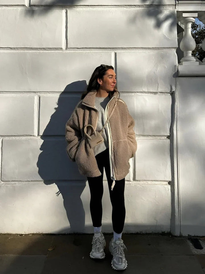 Model kombiniert beige Oversized-Teddyjacke mit schwarzer Leggings und Sneakern