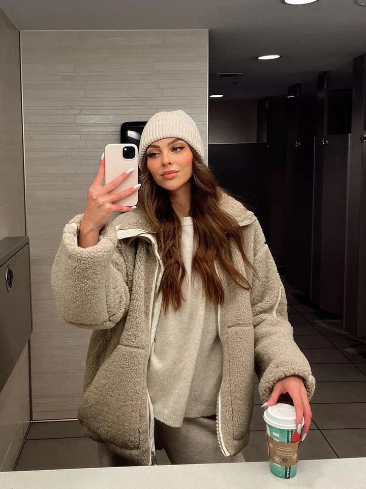 Frau im Spiegelselfie trägt beige Teddyfleece-Jacke mit passender Beanie