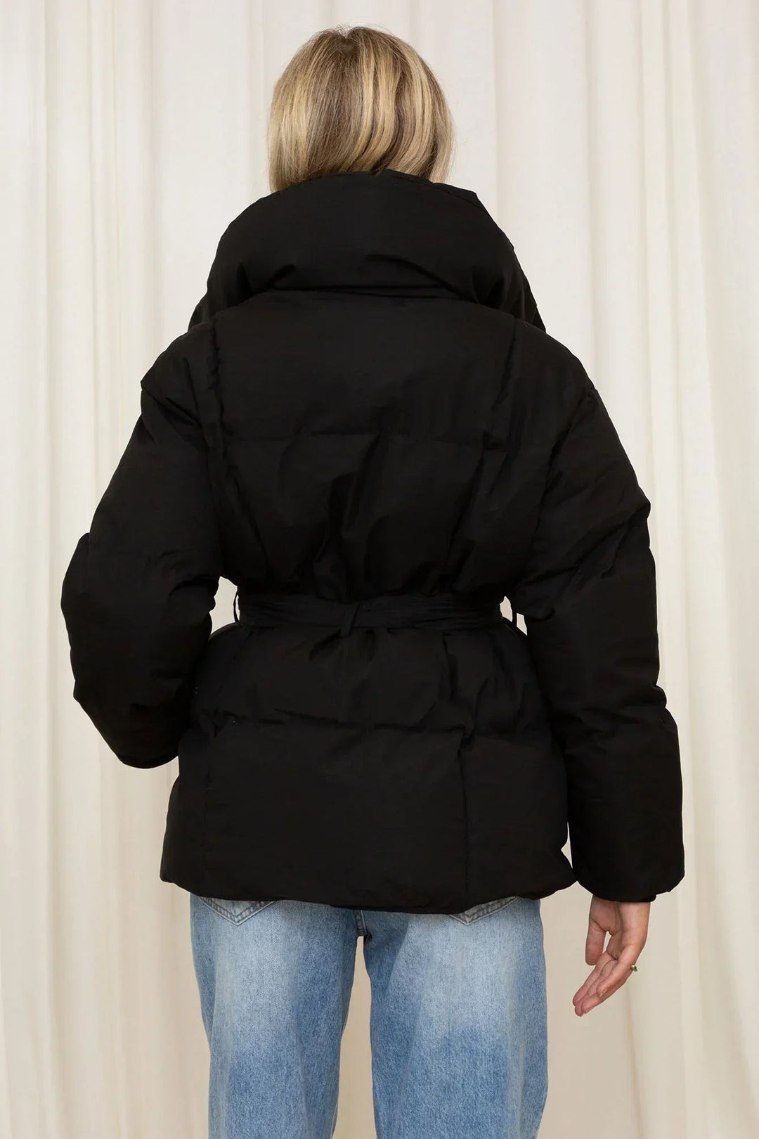 Rückenansicht schwarze Steppjacke mit Stehkragen und gebundenem Gürtel, zu Jeans getragen