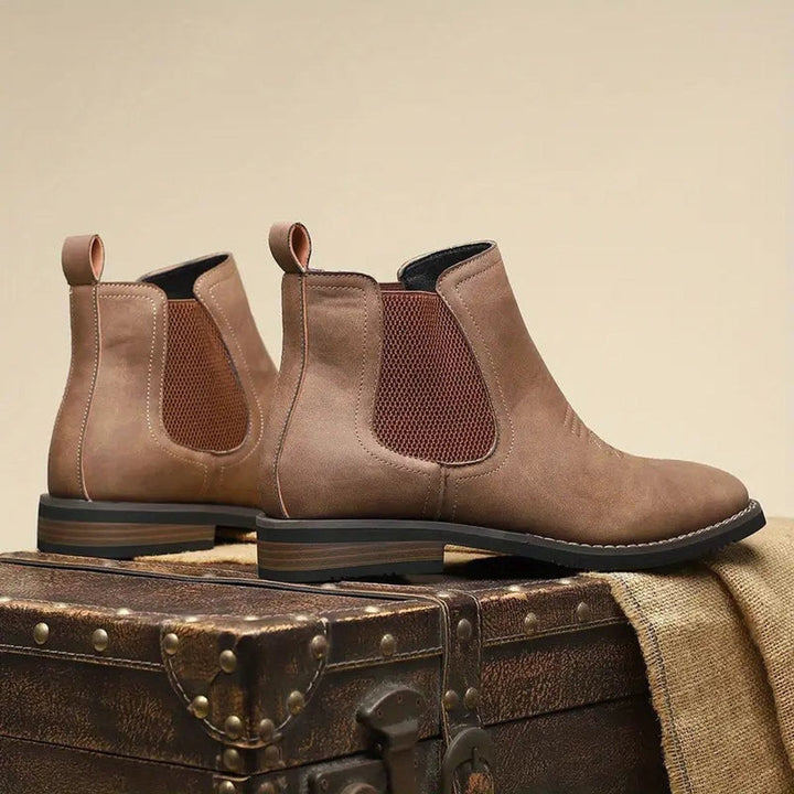 Schwarze Wildleder-Chelsea Boots mit Zierstickerei auf Holzkisten drapiert