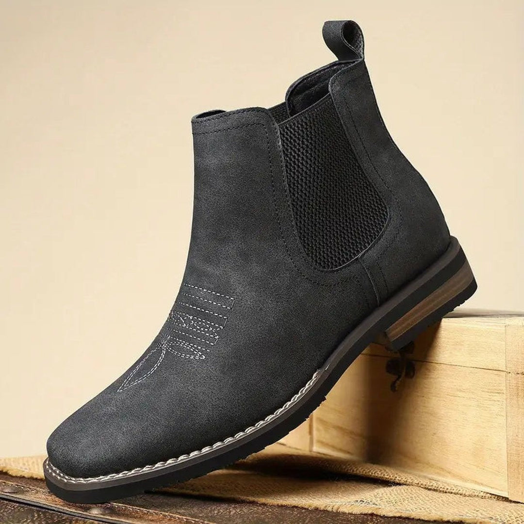 Schwarze Herrenstiefeletten mit Zierstichnaht frontal auf Vintage-Koffer