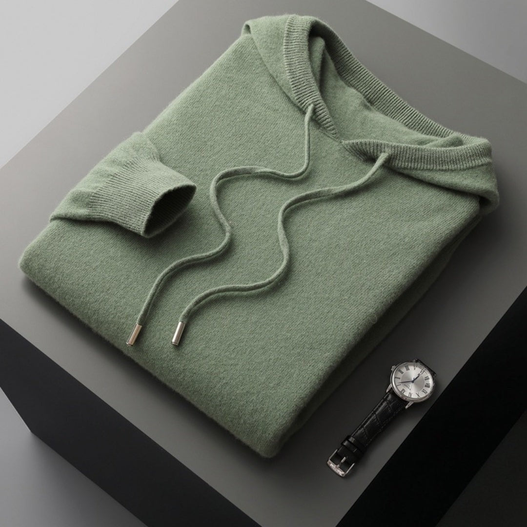 Salbeigrüner Strickhoodie mit Kapuze, gefaltet neben Lederarmbanduhr
