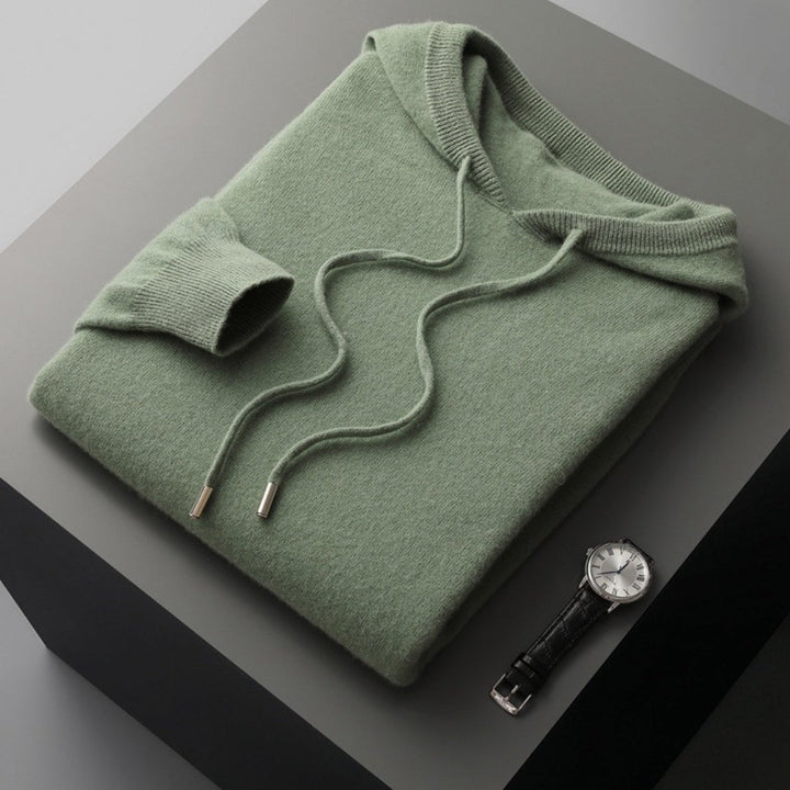 Salbeigrüner Strickhoodie mit Kapuze, gefaltet neben Lederarmbanduhr