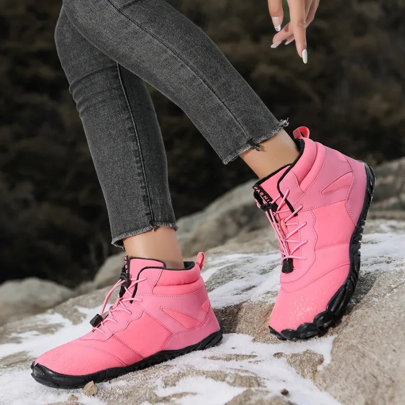 Pinke gefütterte Winterstiefel mit breiter Zehenbox an Frauenfüßen auf Felsen
