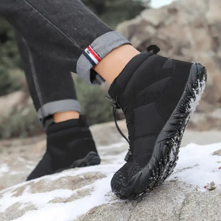 Schwarzer Winterstiefel mit griffiger Profilsohle im Schneelaufschritt auf Felsen