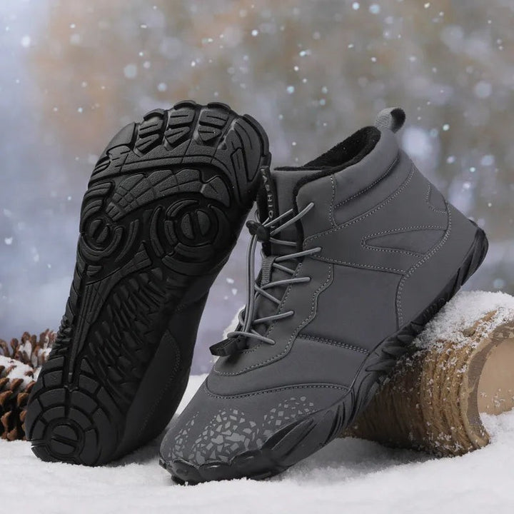 Graue Winterstiefel mit auffälliger Profilsohle und Zugkordel im Schnee präsentiert